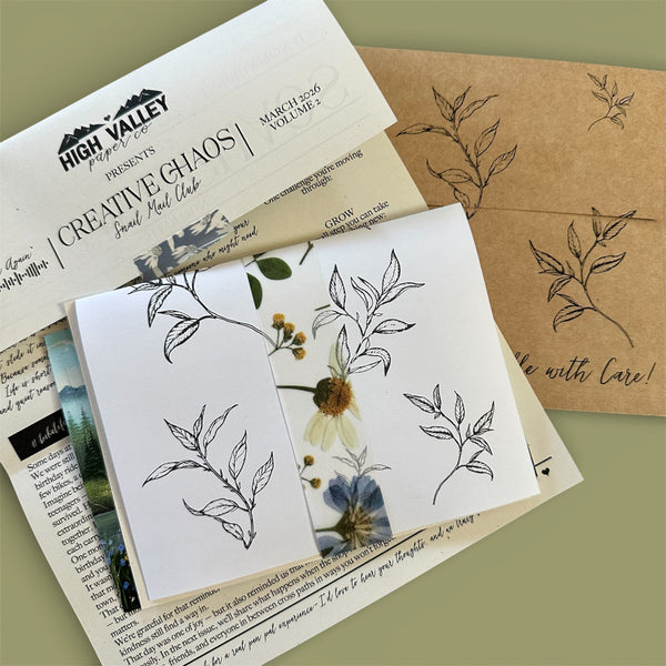 Stationery items including a card with floral designs, an envelope, and a magazine on a green background.